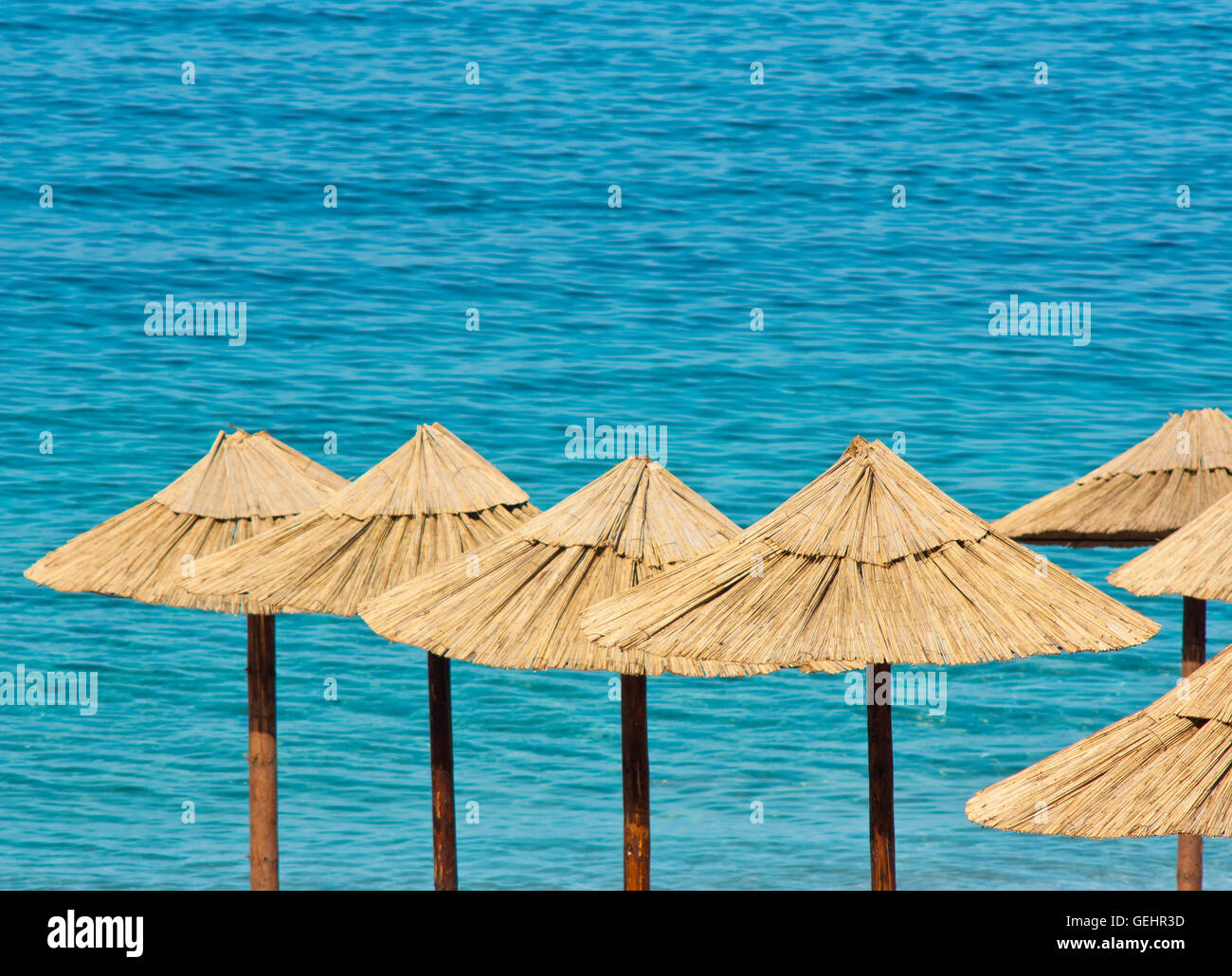Ombrelloni di paglia sulla spiaggia con acqua turchese in background Foto Stock
