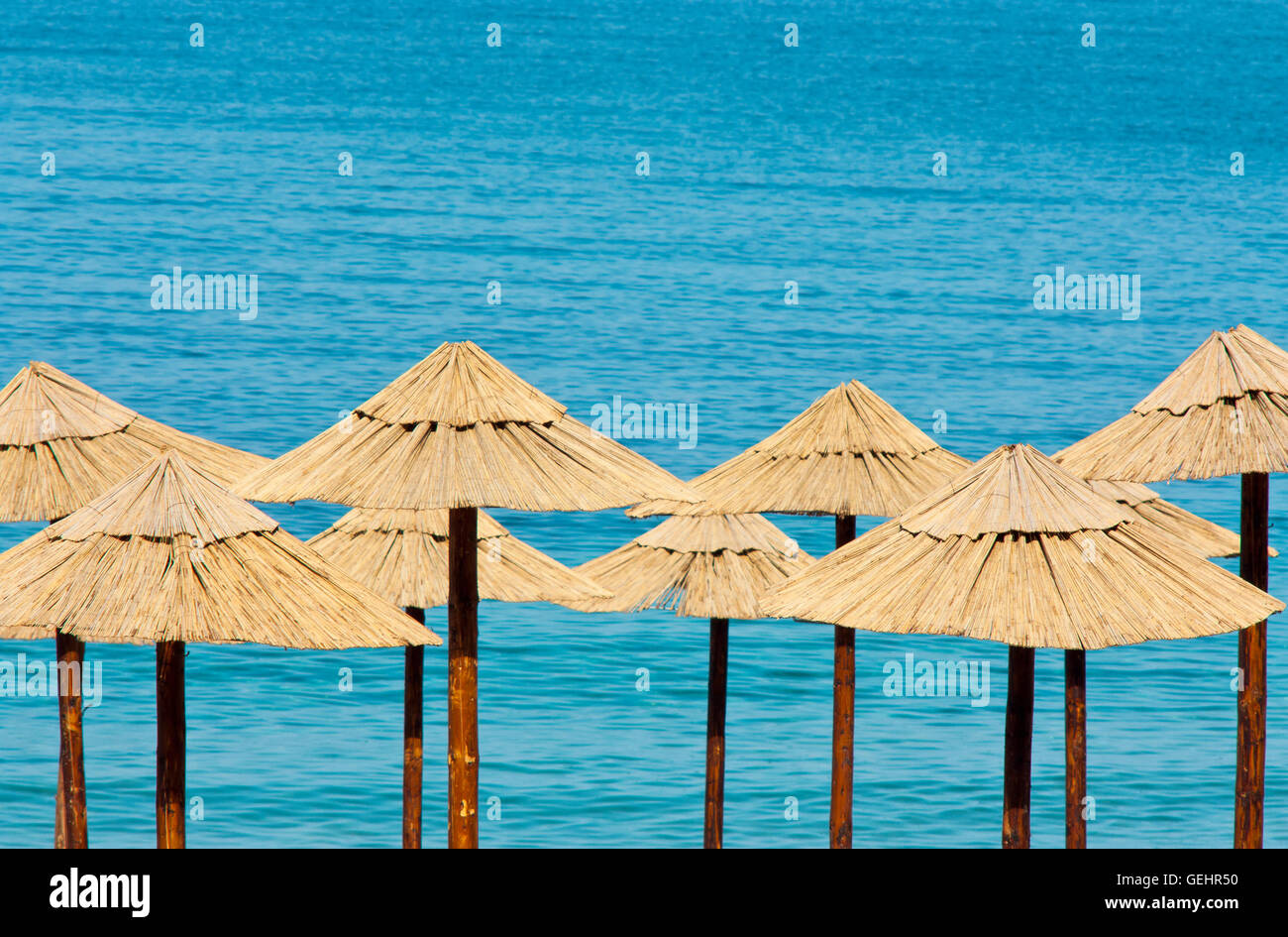 Ombrelloni di paglia su una spiaggia deserta con acqua turchese in background Foto Stock