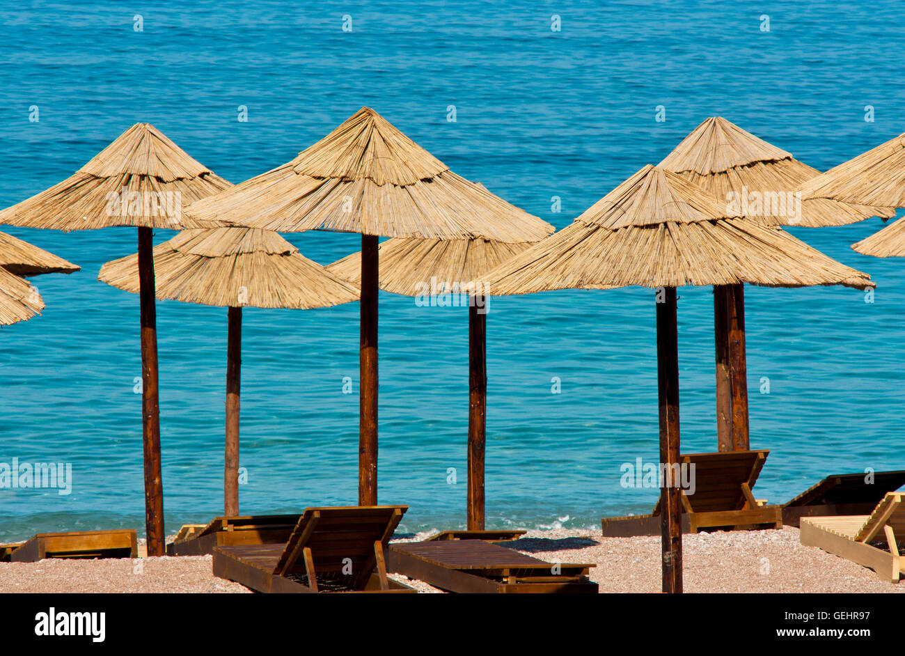 Ombrelloni di paglia e lettini in legno su una spiaggia deserta e acqua turchese in background Foto Stock