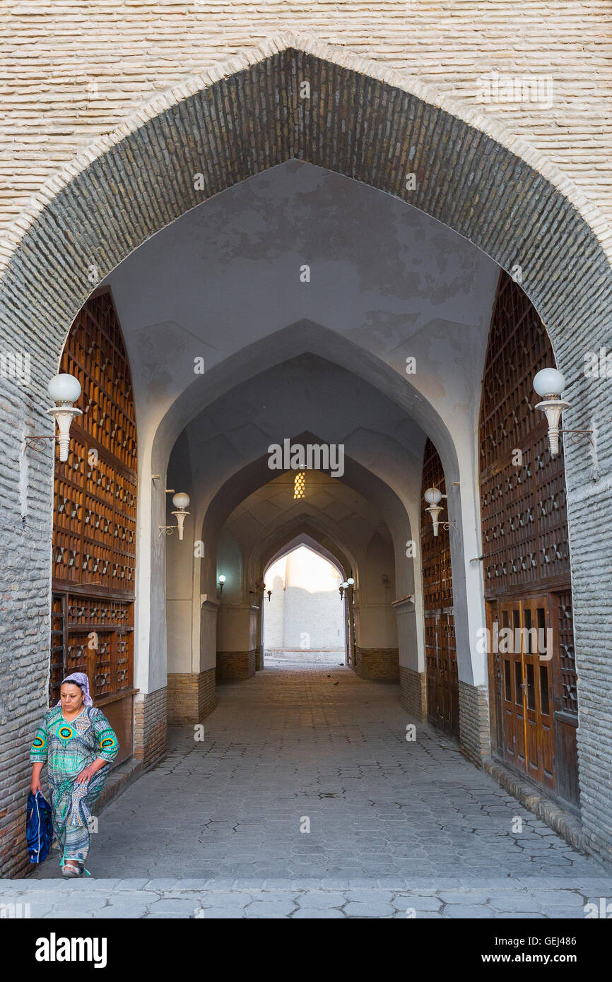 Uzbek donna nel suo abito tradizionale passeggiate attraverso il passaggio arcuato a Bukhara, Uzbekistan. Foto Stock