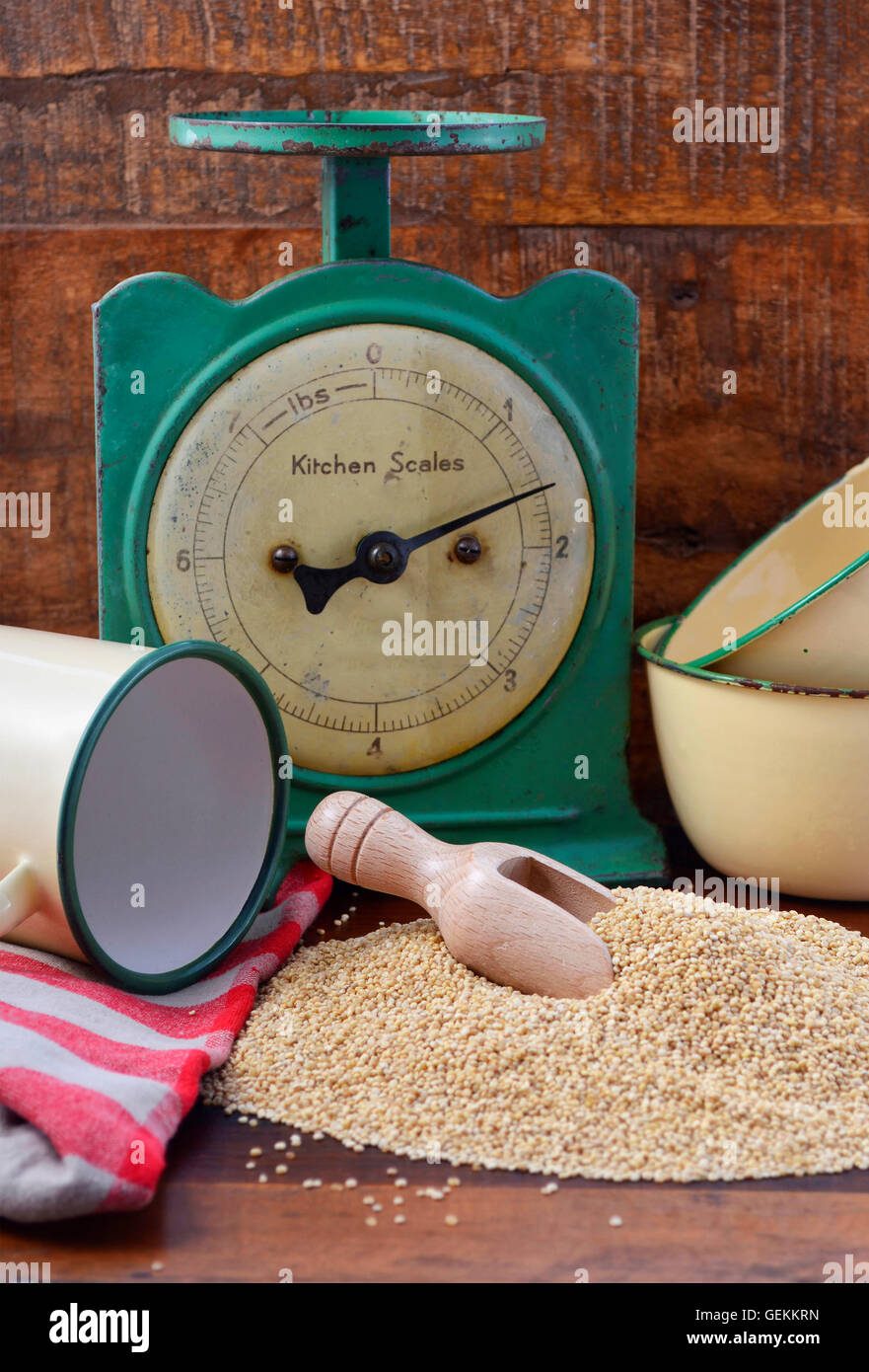 Pila di quinoa granella con la paletta di legno con vintage bilancia da cucina e tin cup coppa sul legno scuro dello sfondo. Foto Stock