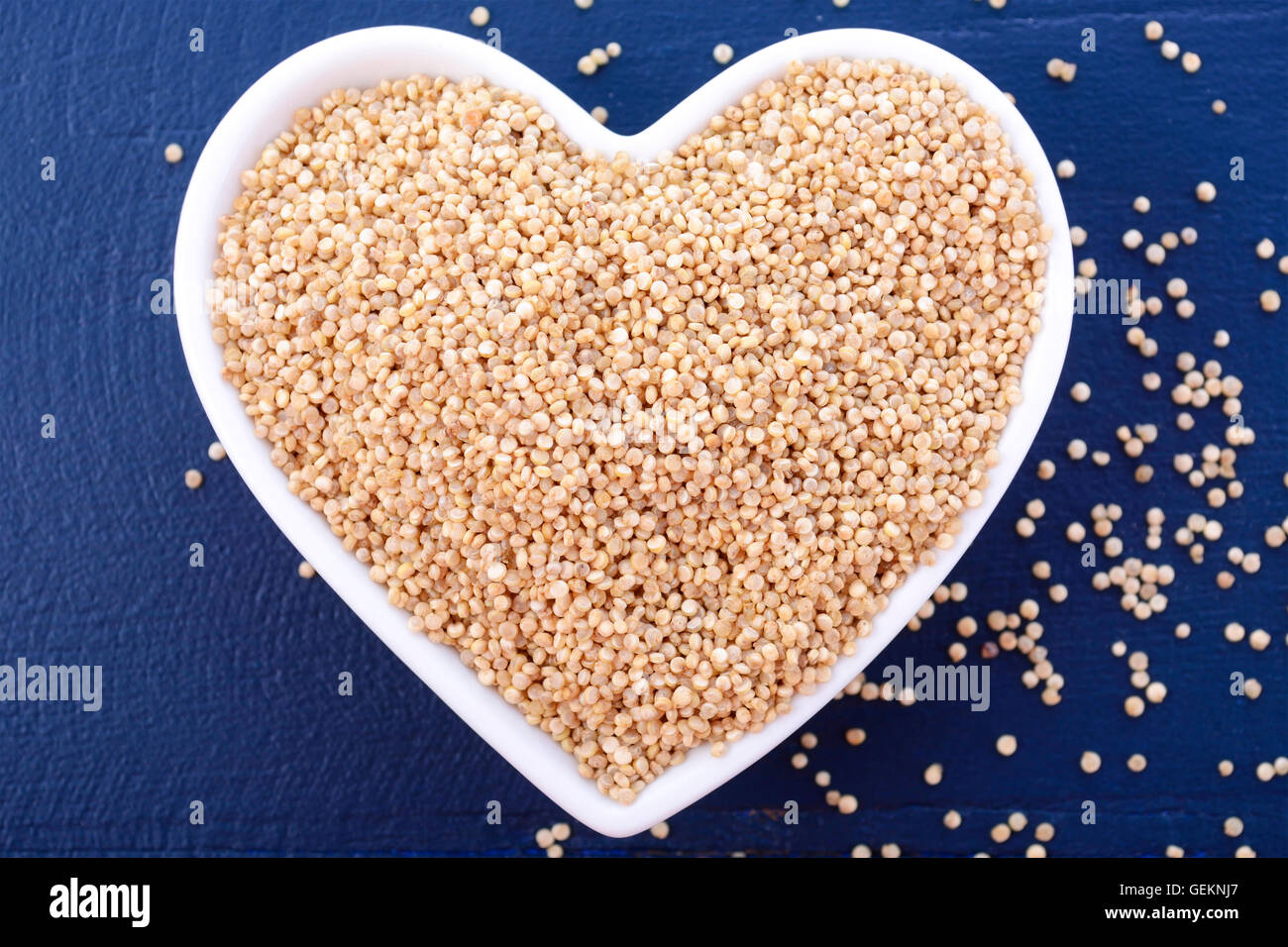 Io amo la quinoa concetto con grano bianco quinoa in bianco a forma di cuore sulla tazza di un blu scuro dello sfondo di legno. Foto Stock