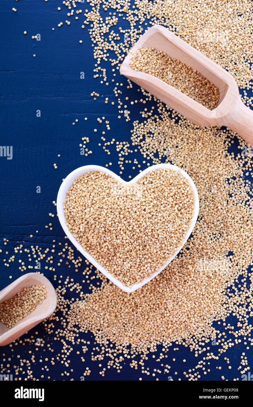 Io amo la quinoa concetto con grano bianco quinoa in bianco a forma di cuore sulla tazza di un blu scuro dello sfondo di legno. Foto Stock