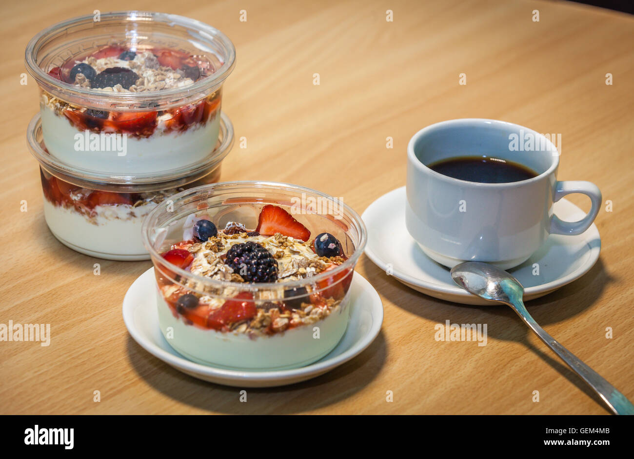 Tazza di caffè e ciotole di preparati di fresco di yogurt naturale con cereali e frutti di bosco Foto Stock