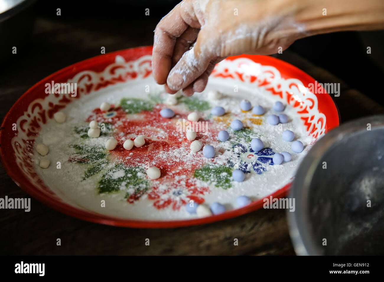 Rivolto verso il basso la mano con le dita stampaggio blu porpora impasto e ponendolo su un piatto di portata con il blu e il bianco da dessert sfere Foto Stock