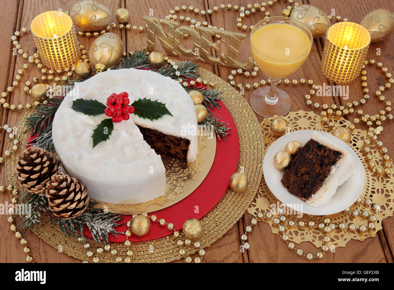 Torta di Natale e slice, con zabaione, agrifoglio bacche, candele, noel glitter firmare e oro ninnolo decorazioni Foto Stock