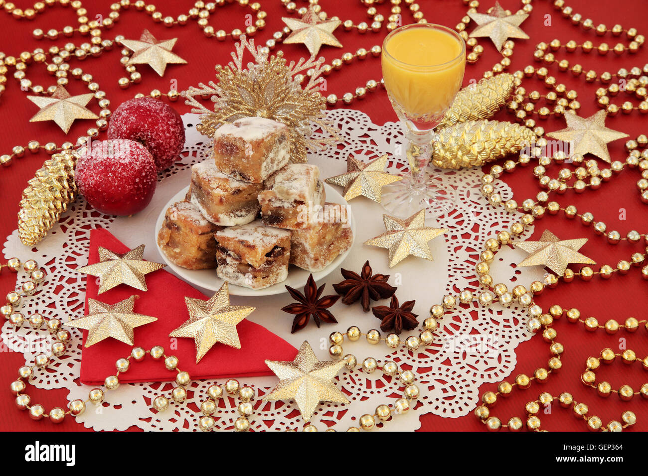 Natale torta stollen morsi, advocaat zabaione e oro ninnolo decorazioni su uno sfondo di colore rosso. Foto Stock