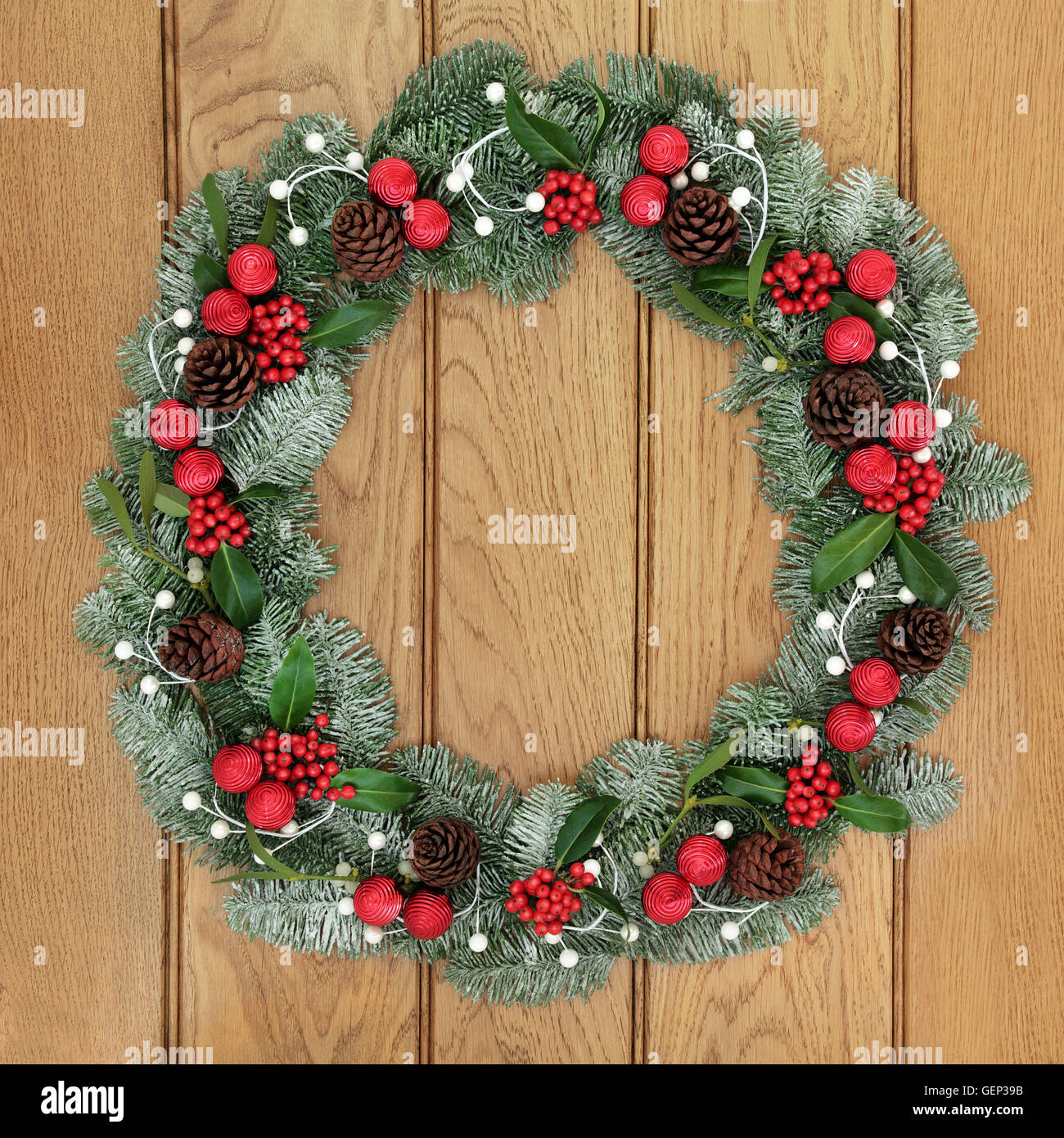 Ghirlanda di Natale decorazione con red ninnolo decorazioni, agrifoglio, coperta di neve blue abete rosso e il vischio su legno di quercia porta. Foto Stock