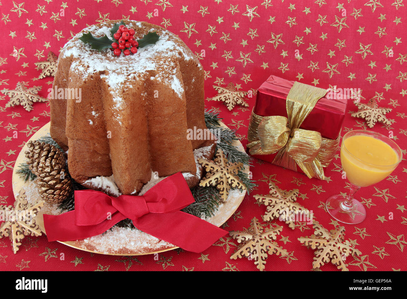 Pandoro torta di Natale con agrifoglio e nastro, uovo nog, il simbolo del fiocco di neve ninnolo decorazioni e confezione regalo su un rosso e oro panno a stella Foto Stock