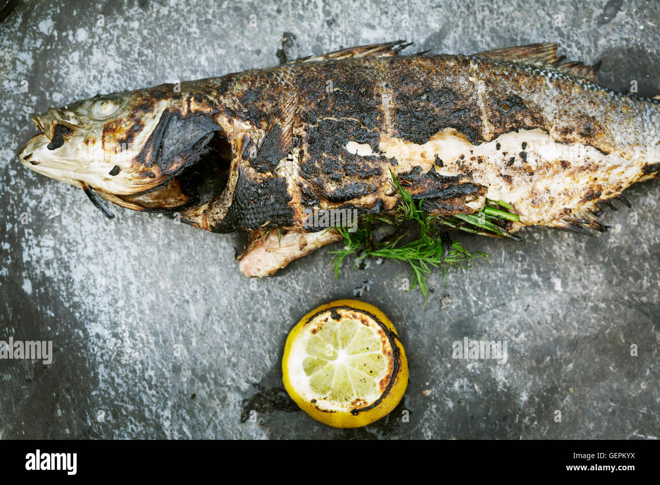 Elevato angolo di visione di un pesce alla griglia con limone e erbe aromatiche. Foto Stock