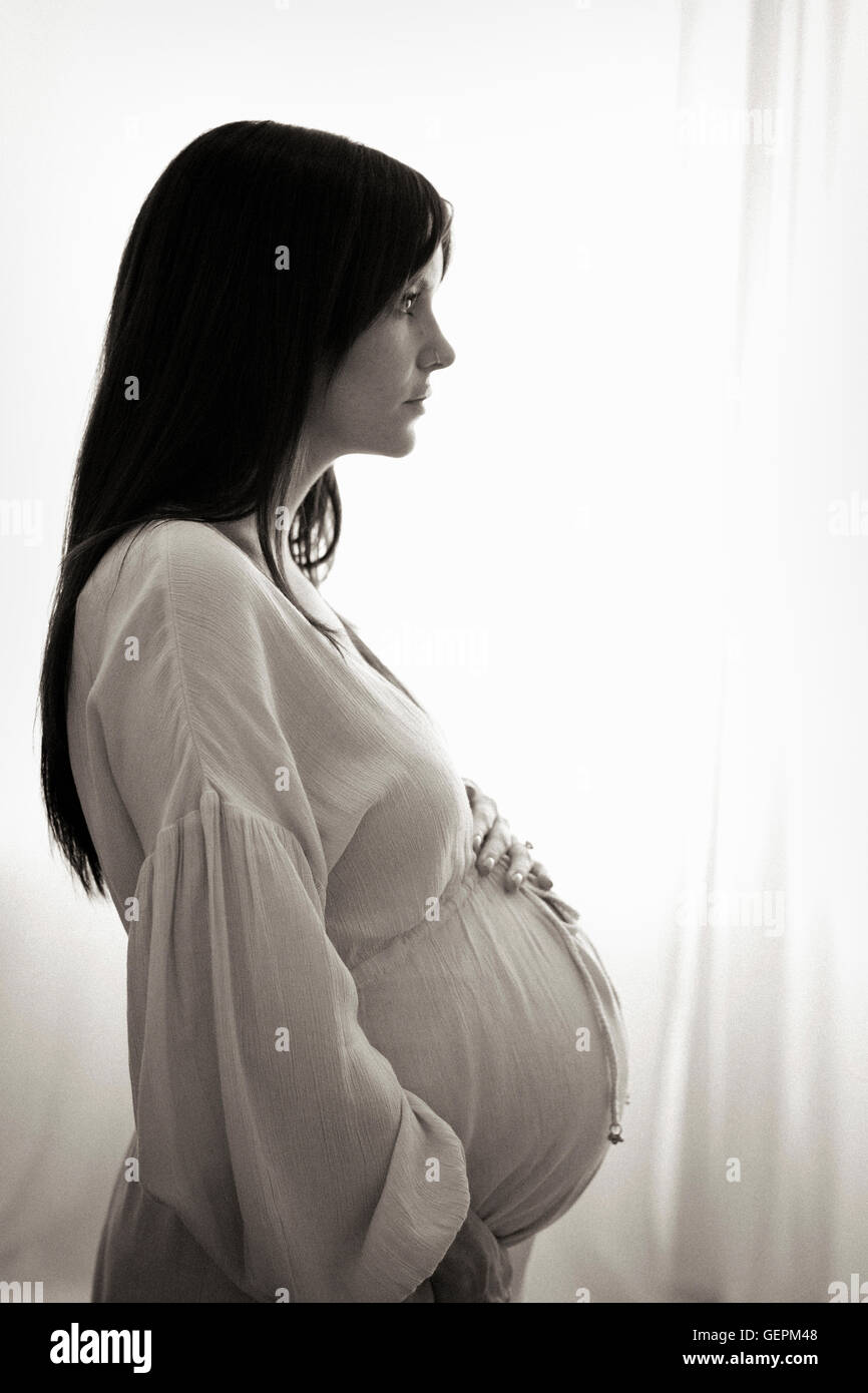 Un fortemente incinta Donna con le mani sul suo stomaco visto di profilo. Foto Stock