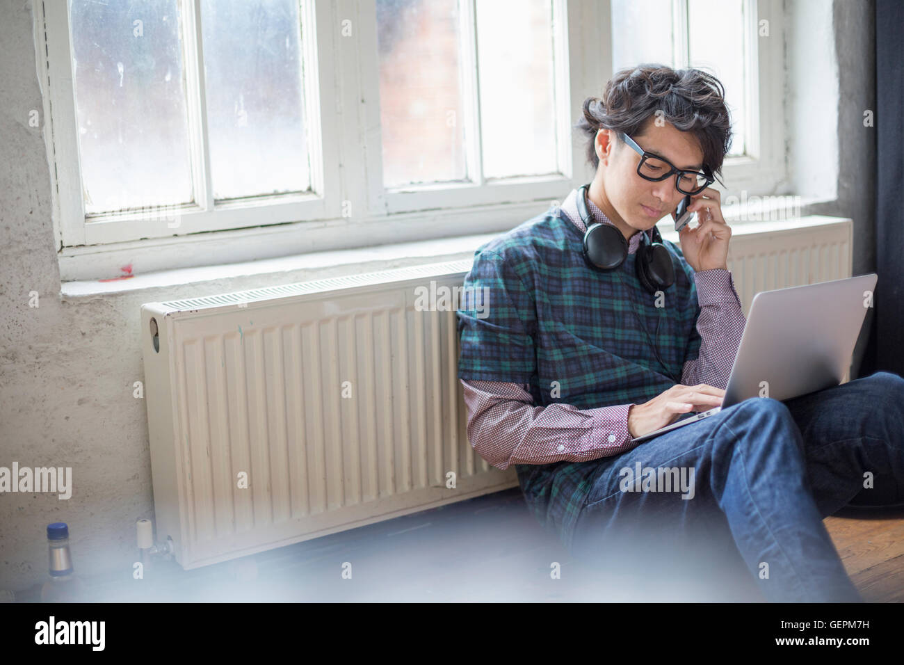 Giovane uomo seduto sul pavimento in una prova studio, utilizzando un computer portatile. Foto Stock