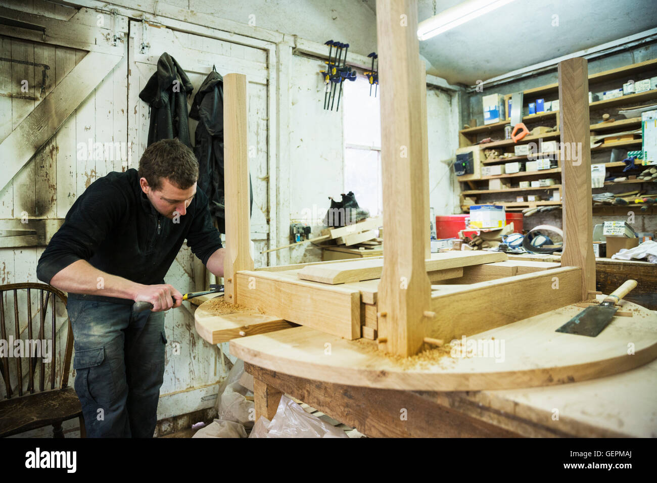 Un uomo in un laboratorio di falegnameria, lavorando sul bordo di un nuovo tavolo in legno con un martello. Foto Stock