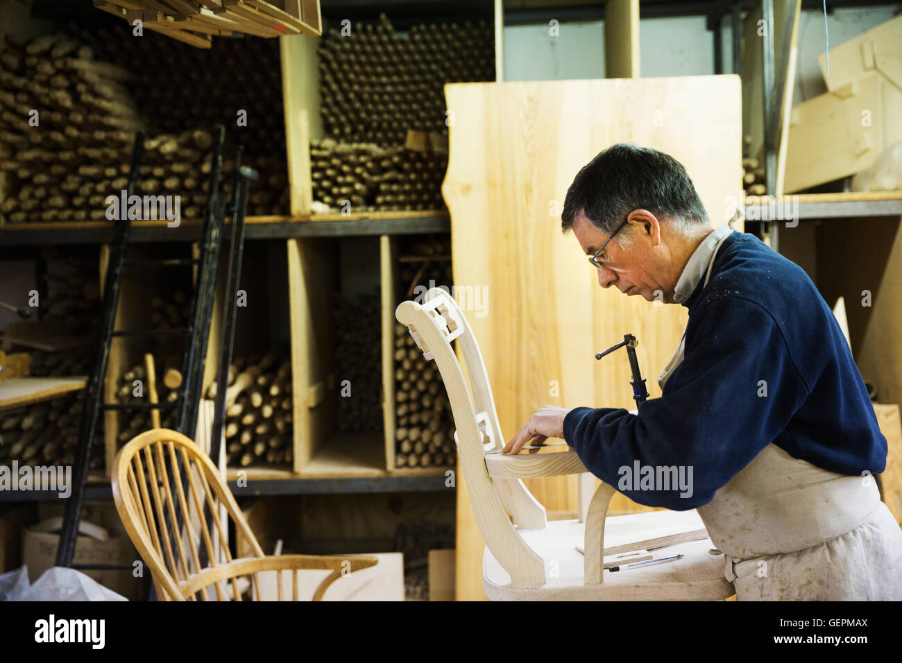 Uomo in piedi in un laboratorio di falegnameria, lavorando su una sedia in legno la marcatura del giunto del bracciolo con una matita. Foto Stock