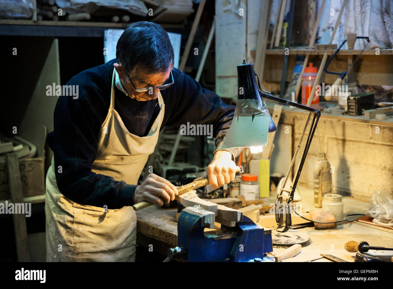 Uomo in piedi in corrispondenza di un banco di lavoro in un laboratorio di falegnameria, lavorando su un pezzo di legno fissato in una morsa da banco con un spokeshave. Foto Stock