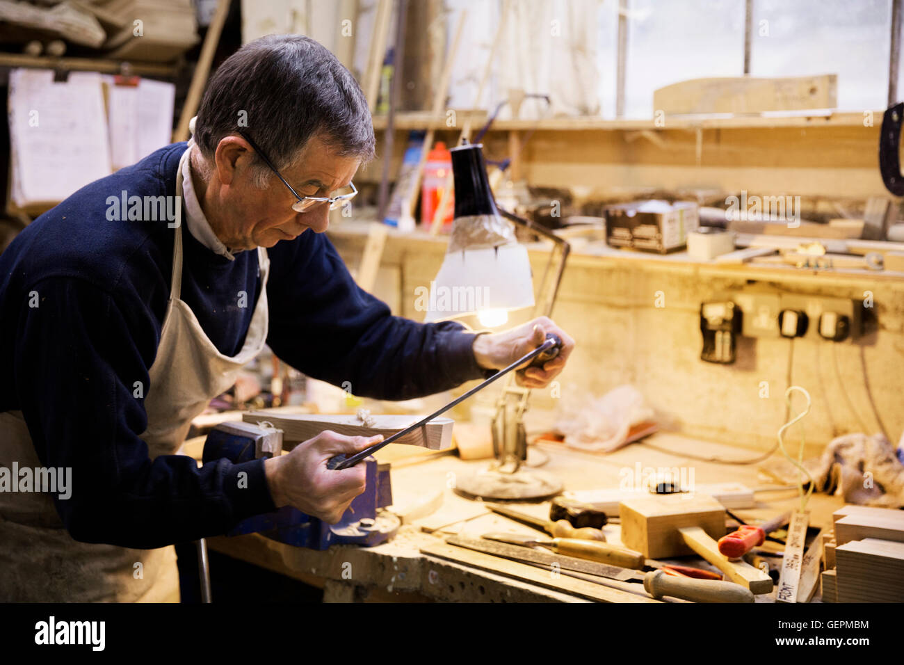 Uomo in piedi in corrispondenza di un banco di lavoro in un laboratorio di falegnameria, lavorando su un pezzo di legno fissato in una morsa da banco. Foto Stock