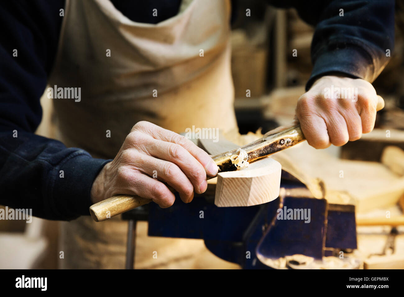 Close up di un uomo in piedi in corrispondenza di un banco di lavoro in un laboratorio di falegnameria, lavorando su una sedia di legno con un spokeshave. Foto Stock
