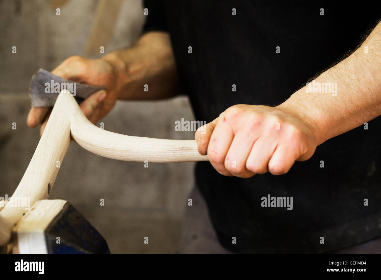 Close up di un uomo la levigazione di un pezzo di legno curvo in un laboratorio di falegnameria. Foto Stock