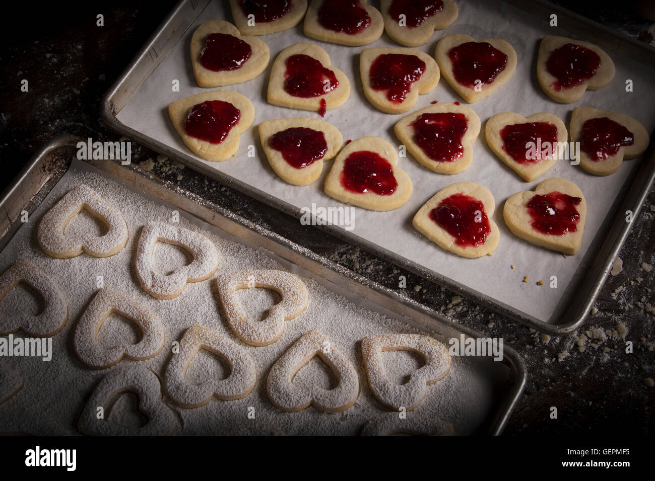 Il giorno di San Valentino la cottura, donna diffusione di confettura di lamponi sul cuore biscotti di forma. Foto Stock
