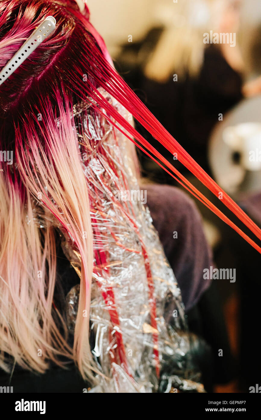 Un capello colorista applicando rosa il colore dei capelli di un cliente del lunghi capelli biondi. Foto Stock