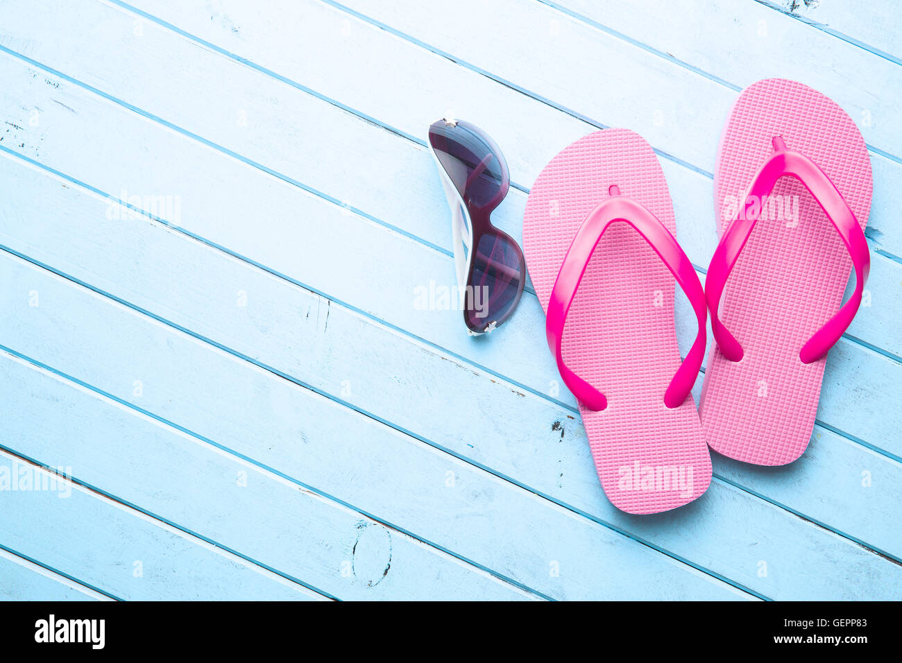 Rosa flip flop e gli occhiali da sole sul pavimento di colore blu. Foto Stock