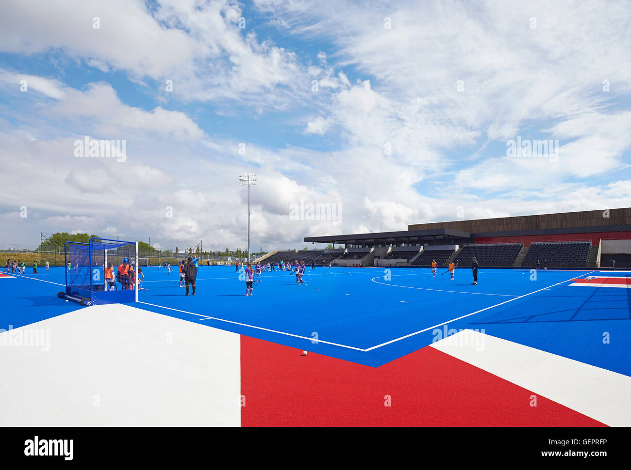 Campo di hockey su prato in blu con i giocatori. Eton Manor - Lee Valley Hockey e il Centro Tennis, Londra, Regno Unito. Architetto: Stanton Foto Stock