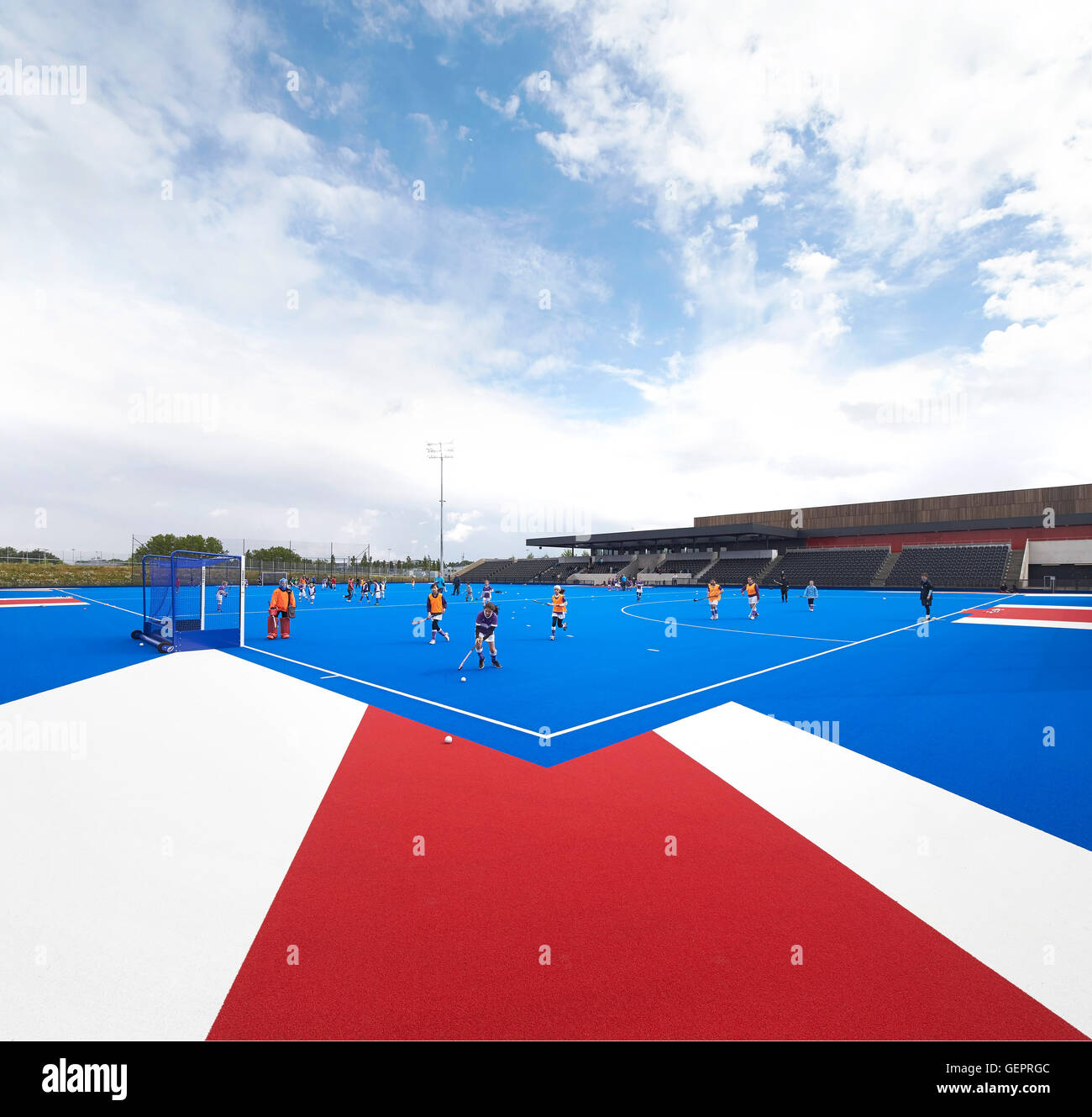 Campo di hockey su prato in blu con i giocatori. Eton Manor - Lee Valley Hockey e il Centro Tennis, Londra, Regno Unito. Architetto: Stanton Foto Stock