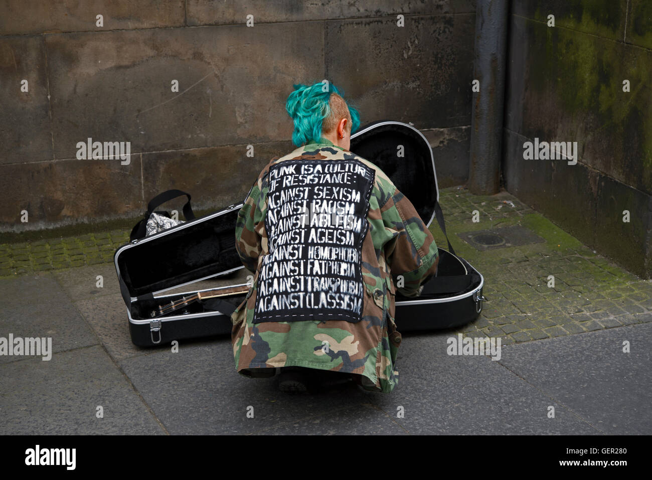 La vista posteriore di una giovane ragazza punk busker mettendo il suo strumento di distanza, la sua giacca elenca Foto Stock