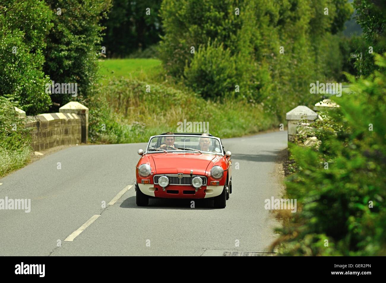 MGB GT roadster attraversando un ponte di pietra sulla strada di un paese su un estate classic car rally in Inghilterra Foto Stock
