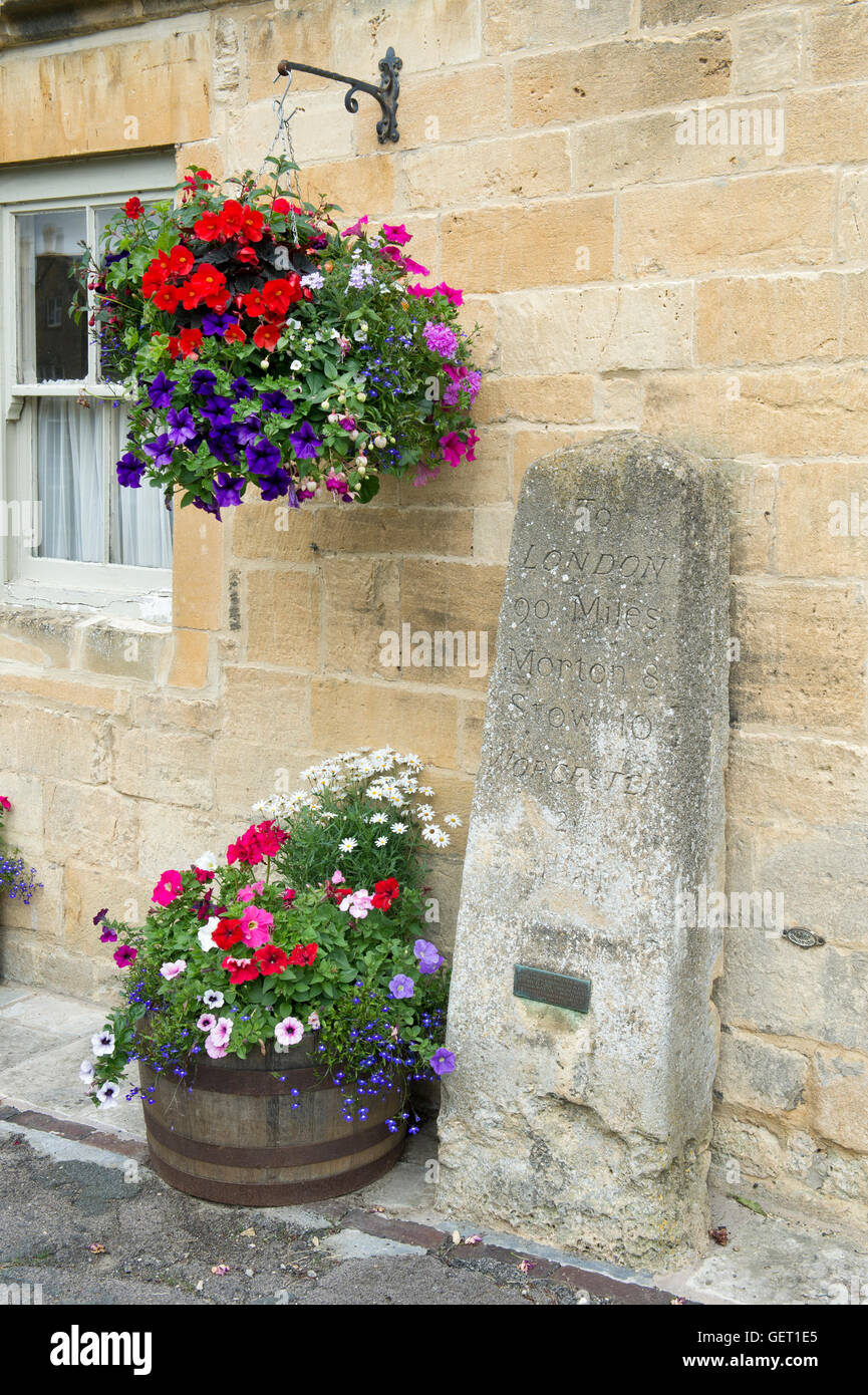 Vecchia pietra miliare appesi a cesto e vasca di fiori nella parte anteriore della casa della fase cardine. Broadway, Cotswolds, Worcestershire, Inghilterra Foto Stock