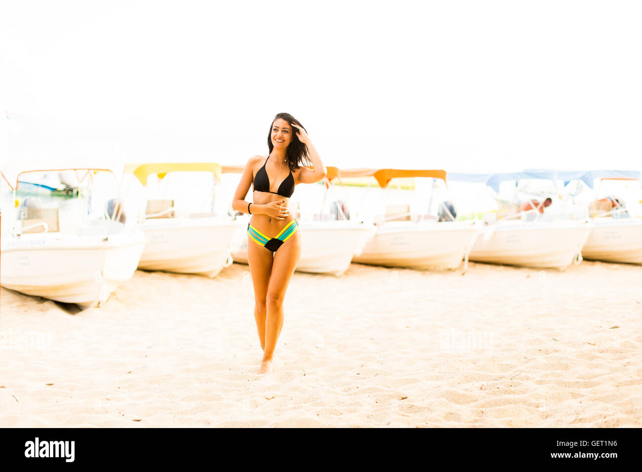 Giovane donna sulla spiaggia sabbiosa con barche in estate Foto Stock