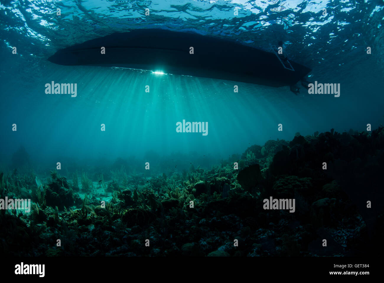 La luce diretta del sole silhouette di una barca al di sopra di una barriera corallina del Mar dei Caraibi. Questa zona è popolare tra gli amanti delle immersioni e dello snorkeling. Foto Stock