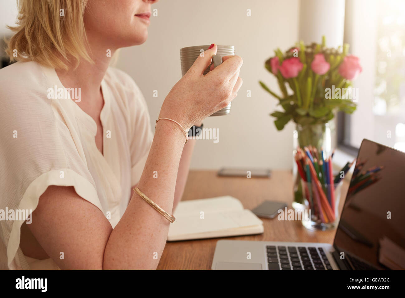 Vista laterale di imprenditrice di bere il caffè mentre è seduto alla sua scrivania. Femmina caucasica avente il caffè mentre si lavora da hom Foto Stock
