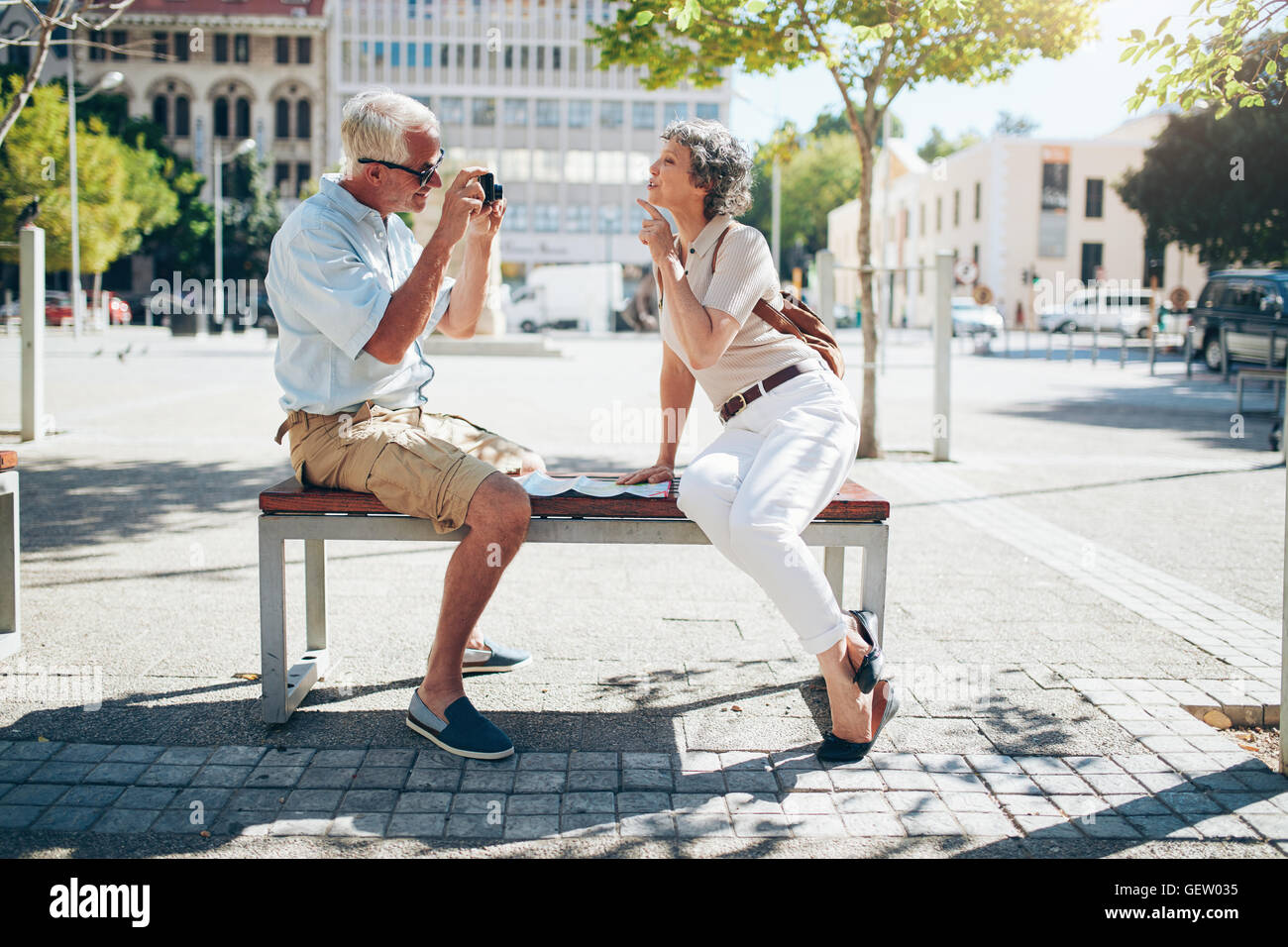 Vista laterale di uomo maturo di fotografare la moglie. Coppia senior seduti all'aperto su un banco a scattare foto di ogni altro con dig Foto Stock