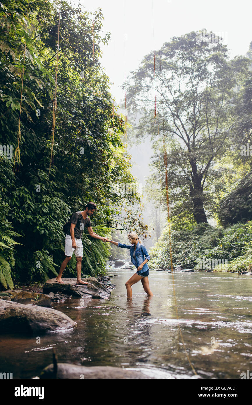 Colpo all'aperto della giovane donna aiuta il flusso di attraversamento. Matura in foresta attraversando il creek. Foto Stock