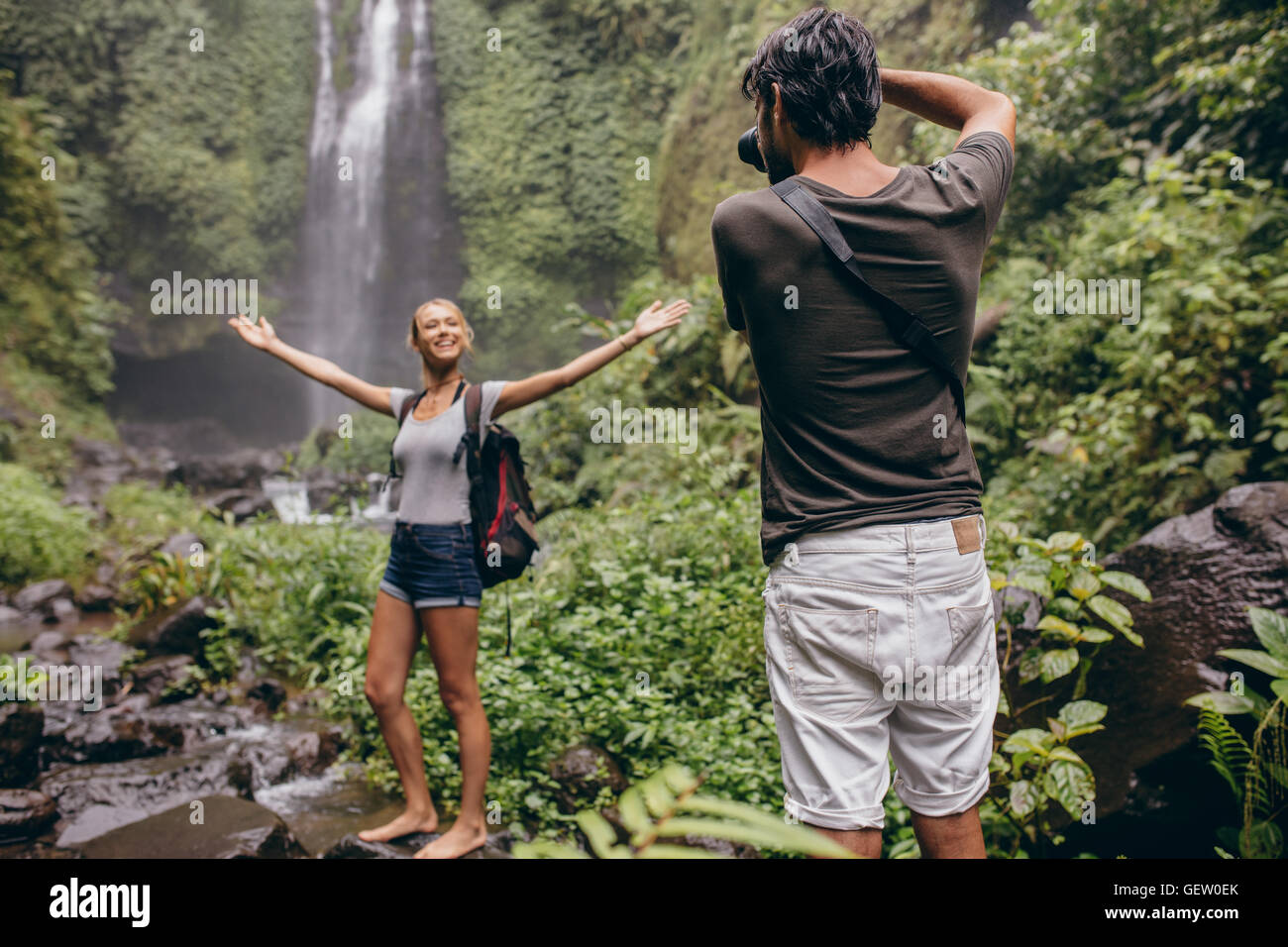 Eccitato giovane donna in piedi di fronte ad una cascata di essere fotografato con il suo fidanzato. Fotografo a scattare foto di donna. Foto Stock