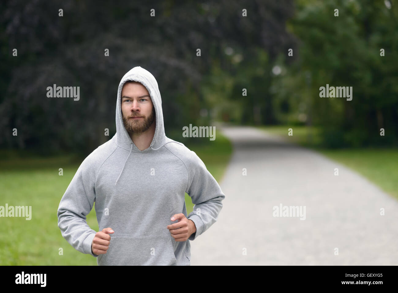 Giovane uomo che indossa una felpa con cappuccio jogging attraverso un parco in una salute e fitness con il concetto di spazio di copia Foto Stock