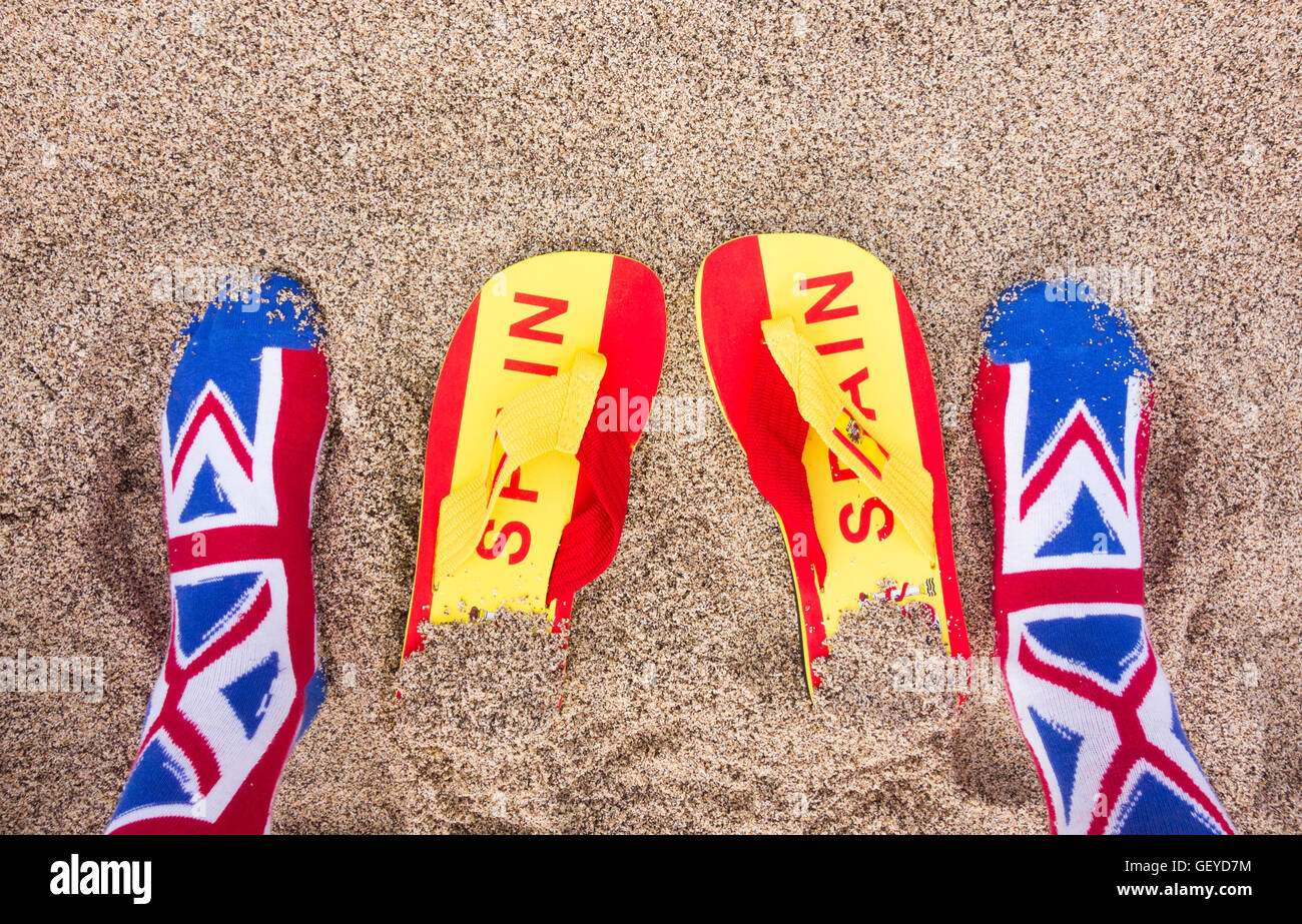 Il turista britannico indossa le calze di Union Jack sulla spiaggia: Bandiera spagnola infradito in sabbia. Brexit, restrizioni di viaggio, libertà di circolazione, UE Foto Stock