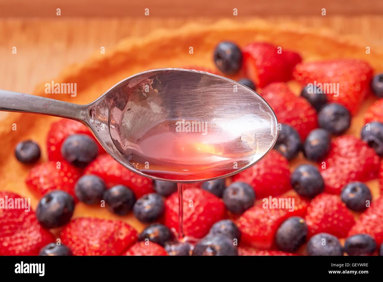 Cucchiaio di colata e di gelatina di caduta su una fragola torta di frutta Foto Stock