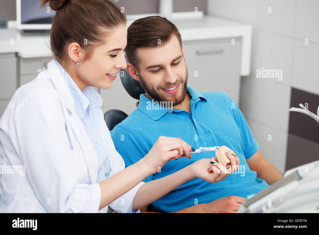 Colpo di una femmina di dentista spiegando al giovane paziente di sesso maschile come spazzola correttamente i suoi denti. Foto Stock
