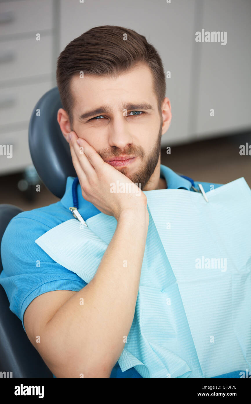 Inquadratura di un giovane uomo con dente dolore mentre è seduto in una poltrona del dentista. Foto Stock