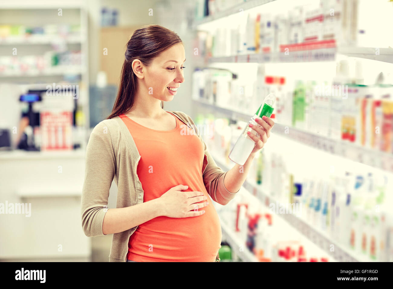 Felice donna incinta scegliendo lozione in farmacia Foto Stock
