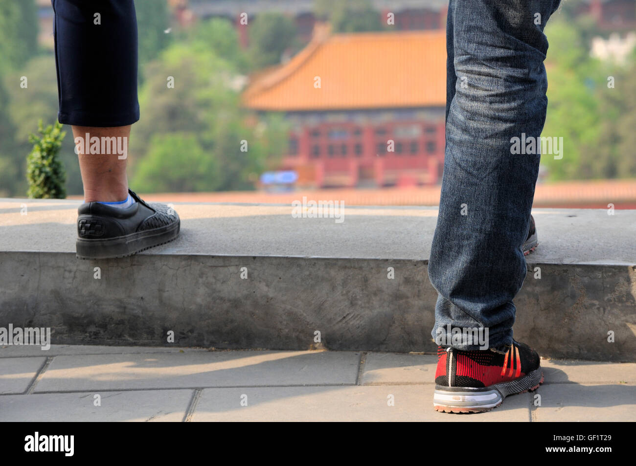 La parte inferiore delle gambe di due uomini stavano in piedi su una parete con uno sfondo sfocato di un edificio cinese all'interno di Jingshan Park di Pechino Foto Stock La parte inferiore delle gambe di due uomini stavano in piedi su una parete con uno sfondo sfocato di un edificio cinese all'interno di Jingshan Park di Pechino Foto Stock