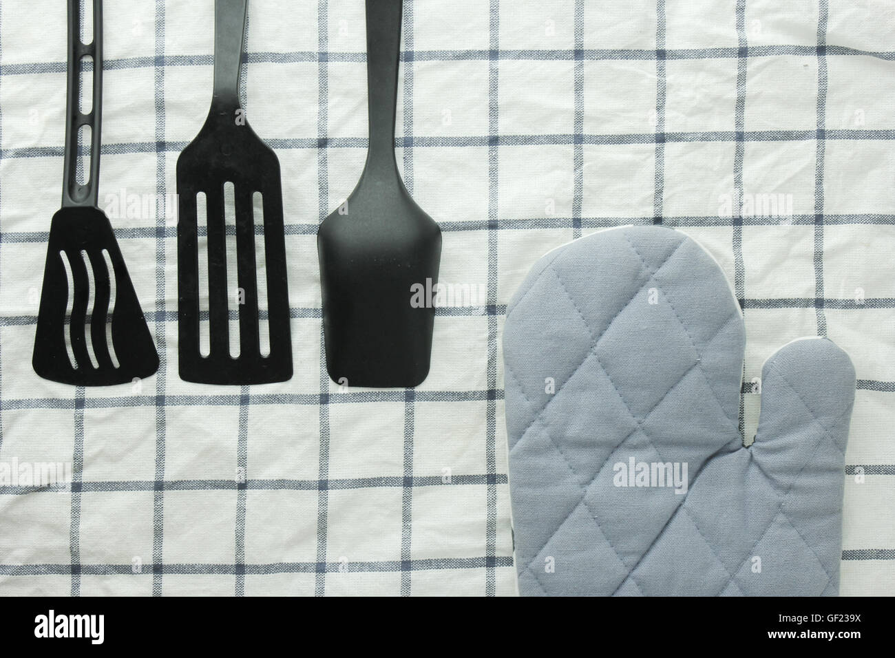Siviera nero, guanto da forno e spade di padella sul tavolo bianco Foto Stock