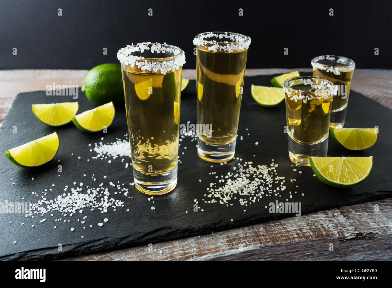 Tequila scatti con calce sulla pietra nera dello sfondo. Forte bere alcool. Oro tequila messicana scatti. Foto Stock