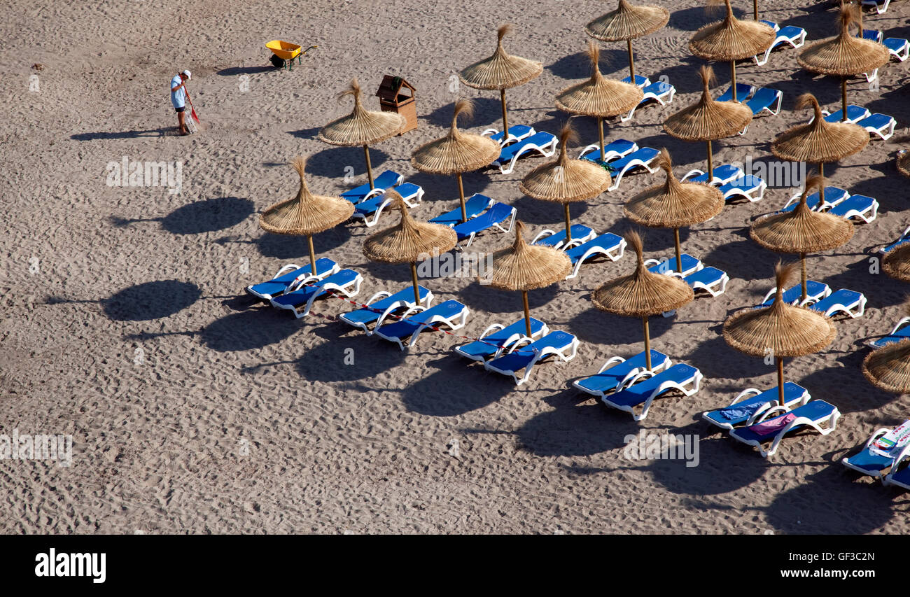 Un uomo che pulisce la spiaggia di mattina presto, prima di arrivare ai bagnanti, in Sant Elm, Mallorca, Spagna Foto Stock