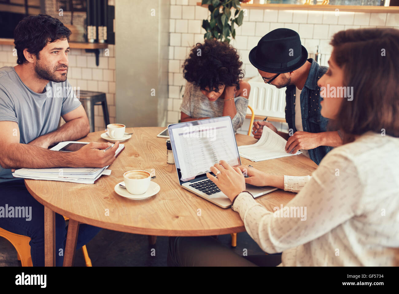 Team di persone creative seduto in un bar con alcuni documenti e laptop. Giovani uomini e donne in un coffee shop per meetin aziendali Foto Stock