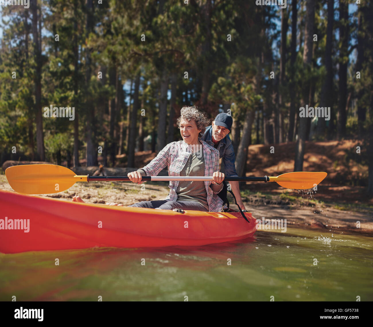 Ritratto di felice coppia matura divertirsi sul lago. Donna canoa kayak con uomo spingendo da dietro su un giorno d'estate. Foto Stock