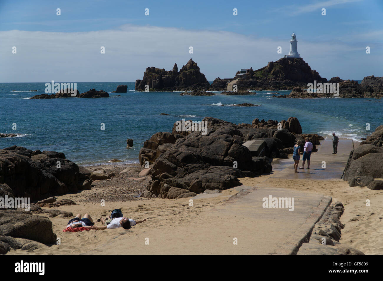 I turisti rilassarvi su una porzione di spiaggia di sabbia con la Corbiere Lighthouse in background,Jersey,Isole del Canale Foto Stock