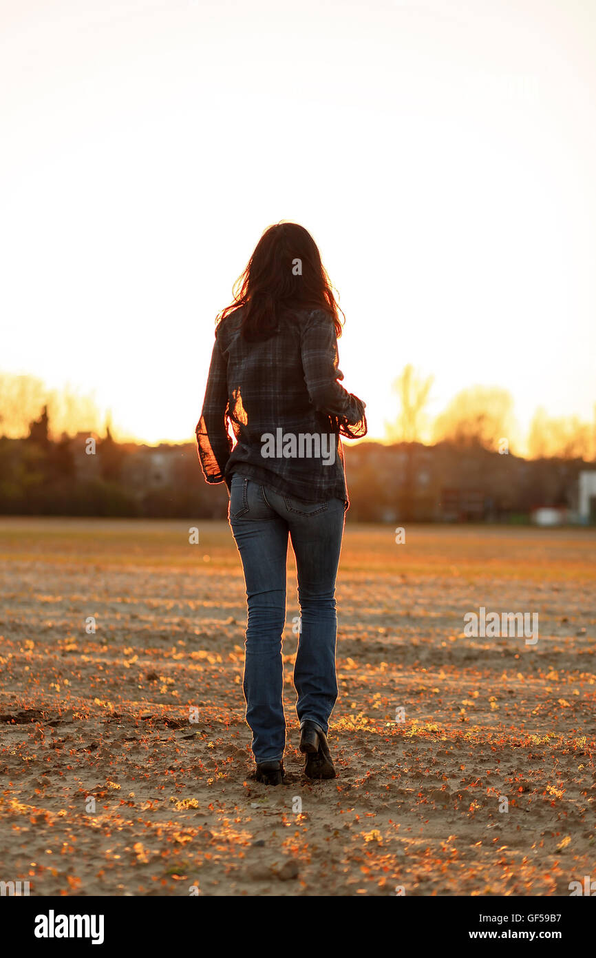 Giovane donna con capelli lunghi da dietro a camminare su un terreno arato al tramonto Foto Stock